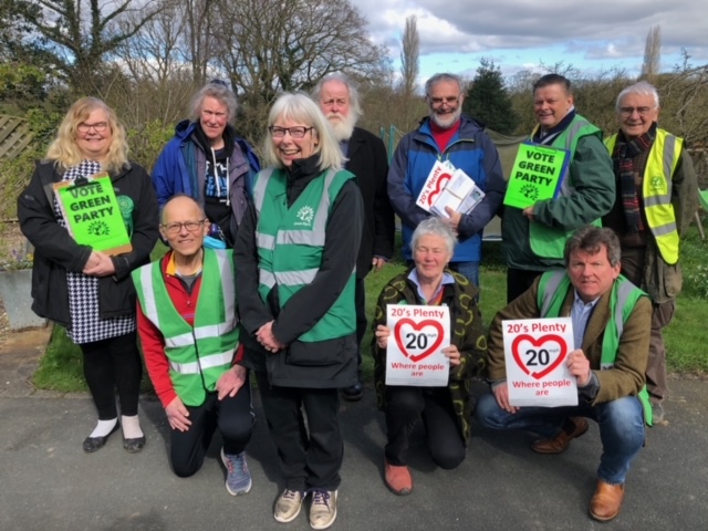 Green Party campaigners in a group huddle holding up posters of "20's Plenty"