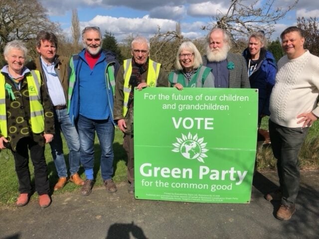 Green Party campaigners holding up a large placard that states "For the future of our Children and Grandchildren, VOTE Green Party for the Common Good"